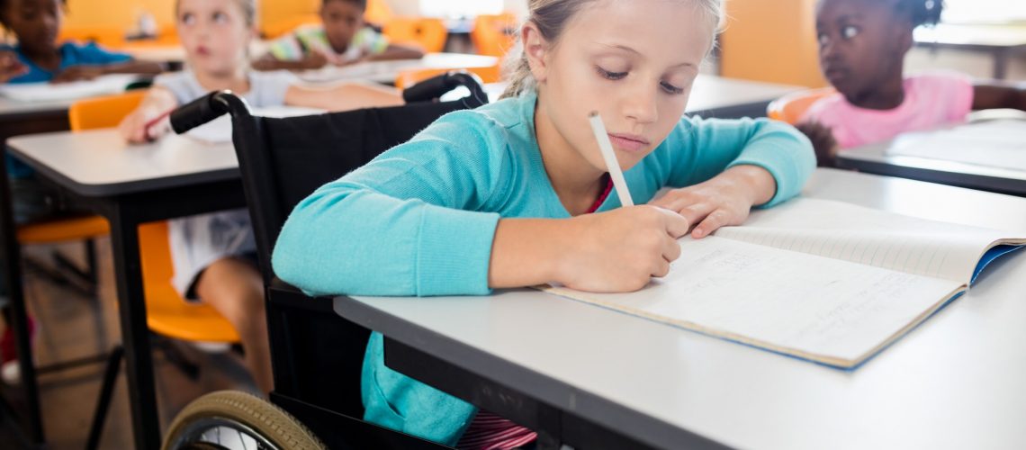 Portrait of a cute pupil in wheel chair working at desk